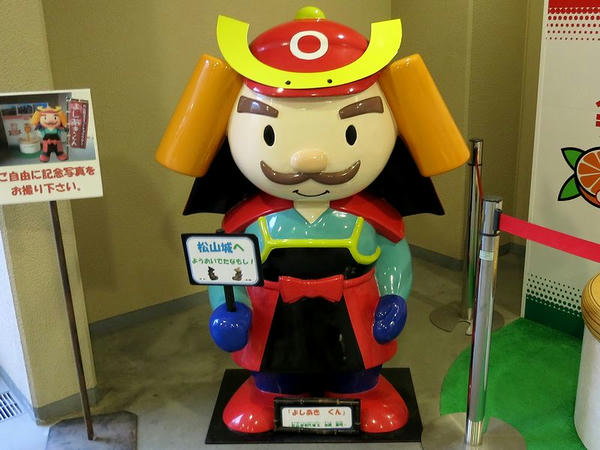 「松山城へようおいでたなもし！」の看板を持つよしあきくん