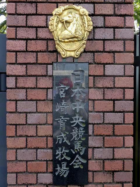 門柱に掲げられた「日本中央競馬会宮崎育成牧場」のプレートとエンブレム