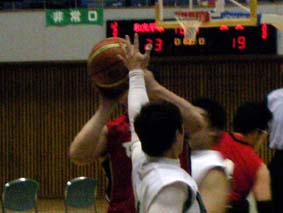 赤いユニフォームの選手がシュートをはなつところ_白いユニフォームの選手が前でプレッシャーをかけているところ