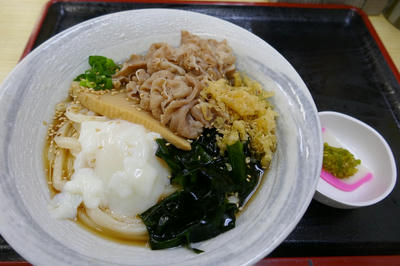 肉、たけのこ、温泉卵、わかめ、天かす、ねぎが載ったぶっかけうどん。横の小皿には薄切りかまぼこの上に柚子胡椒が載っている。