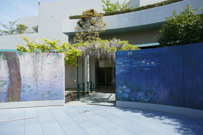 太陽の下、壁一面がモネの睡蓮の絵になっている広場。入口が藤棚になっている。